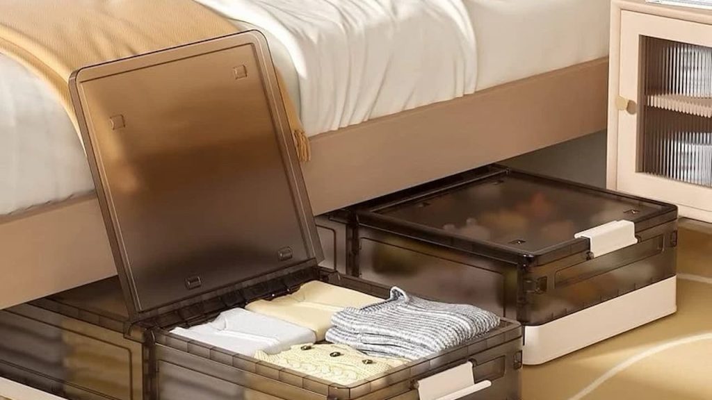 Transparent brown plastic storage boxes, placed under a beige bed, one box open showing neatly folded clothes, ideal for under-bed storage, nearby light wood nightstand with shelves, tidy and organized bedroom space, soft lighting