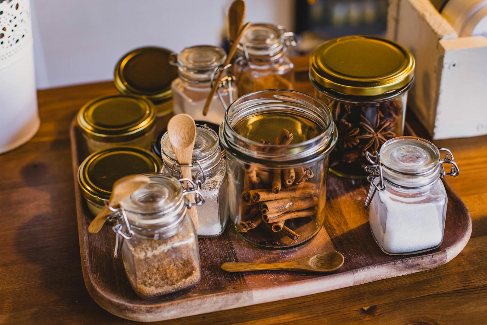 Glass jars filled with spices and kitchen ingredients arranged on a wooden tray.