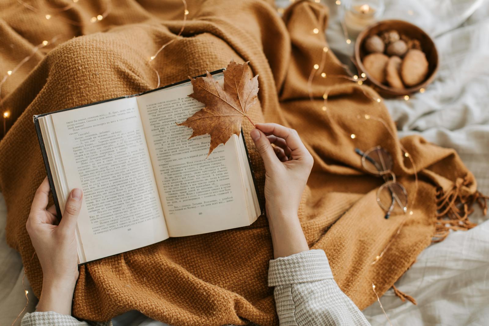 A cozy autumn scene with a book, warm blanket, and cookies for a relaxing reading atmosphere.