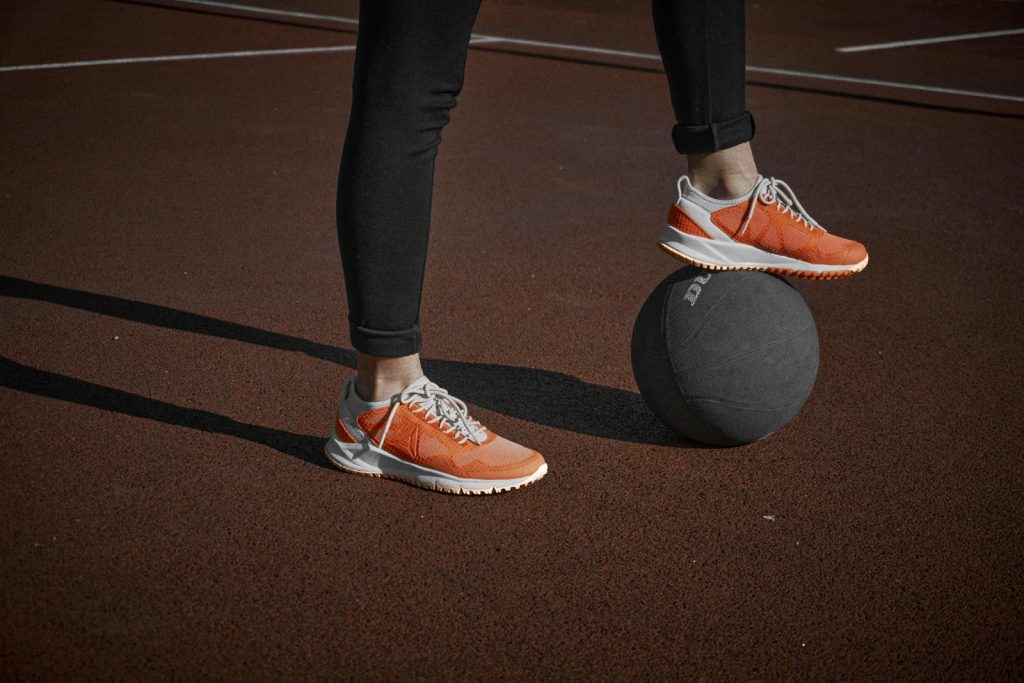 Close-up of an athlete in orange sneakers balancing on a ball on an outdoor court.