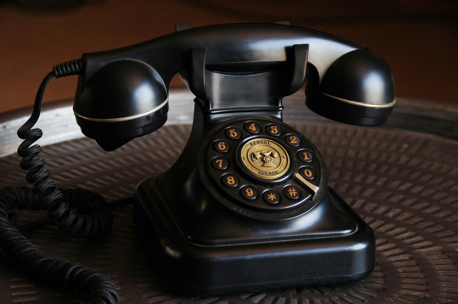 Close-up of a classic black vintage rotary dial telephone on a textured table.