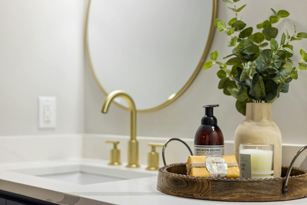 Elegant bathroom featuring a modern gold faucet, large round mirror, and decorative elements on a countertop.