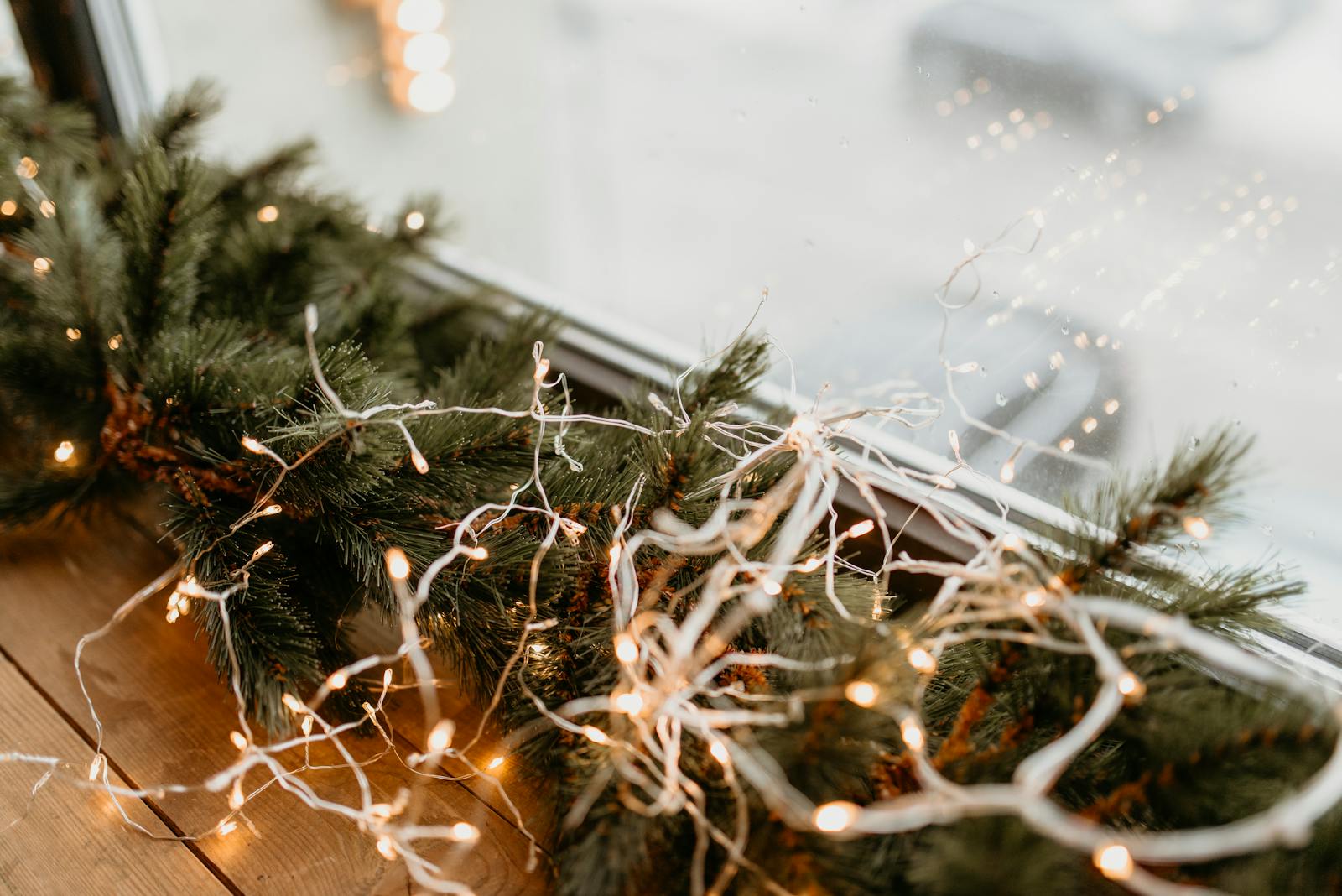 Close-up of twinkling string lights wrapped around pine garland on a window ledge, creating a festive winter ambiance.