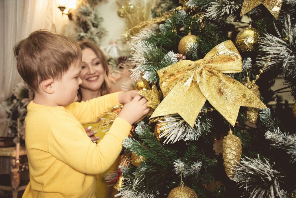 a woman and a child are decorating a christmas tree