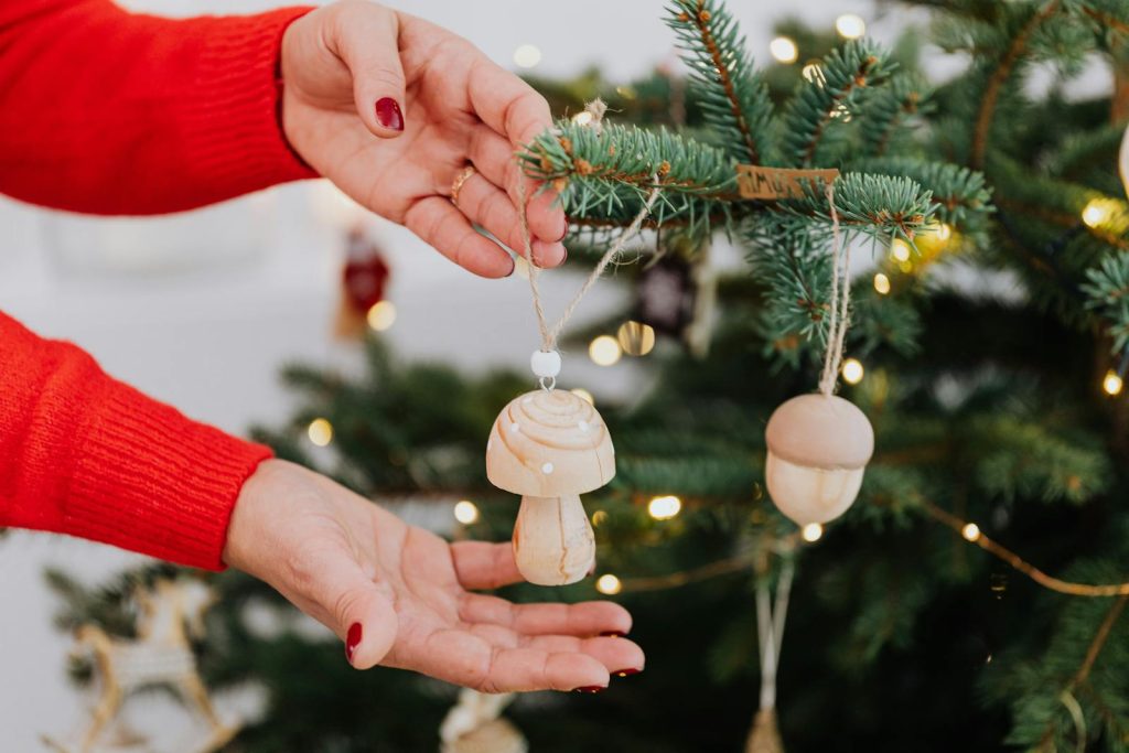 Hands decorating a Christmas tree with wooden mushroom ornaments, adding a rustic charm.
