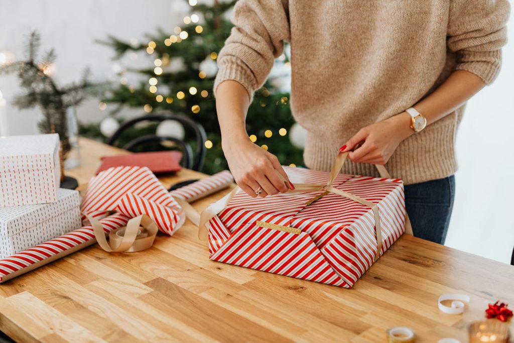 A woman wrapping gifts by a Christmas tree, spreading holiday cheer.
