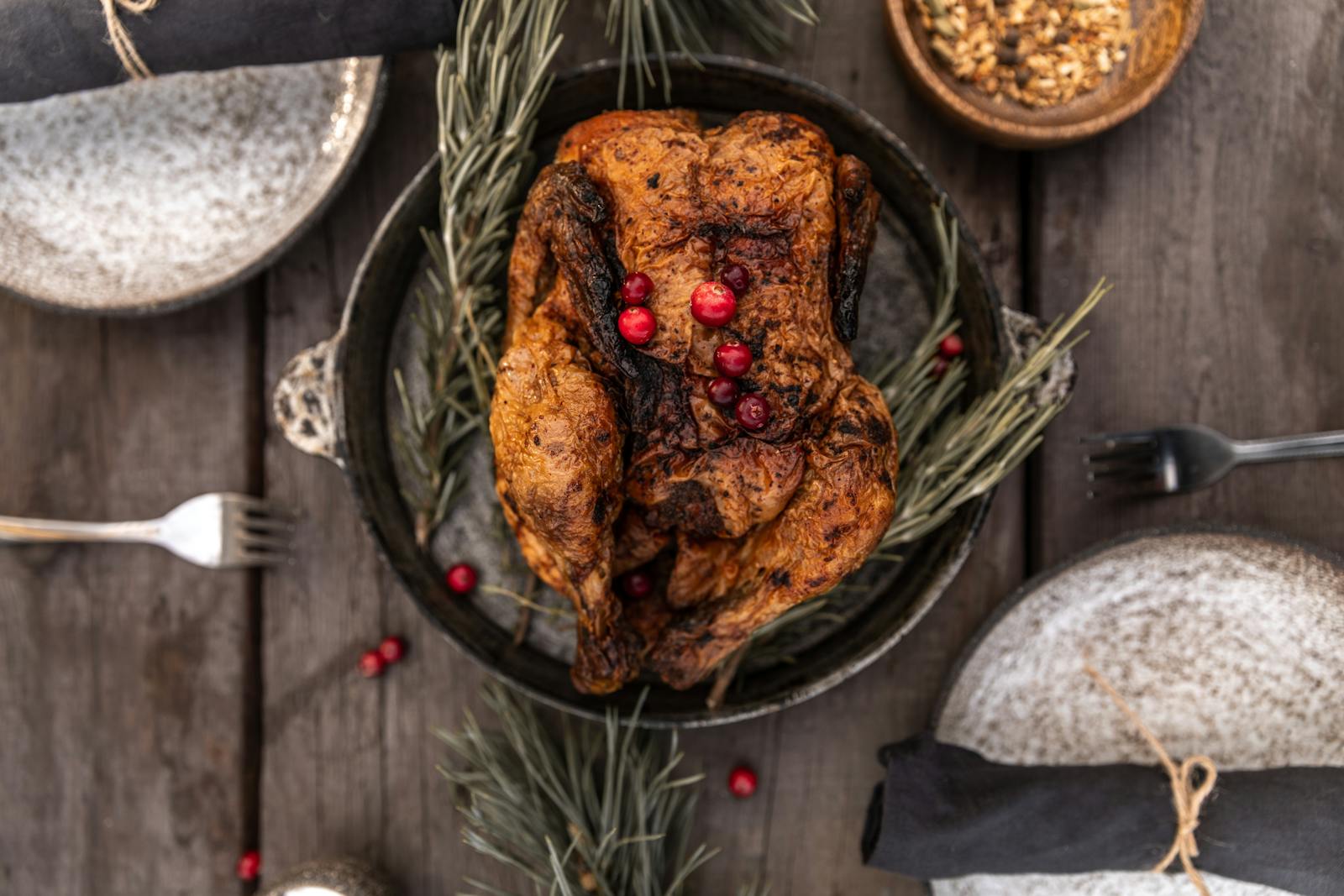 A beautifully roasted turkey garnished with cranberries on a wooden table setting.