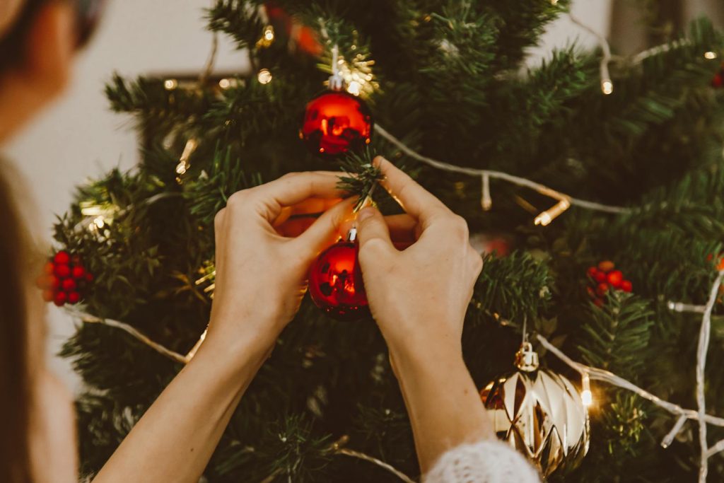 Close-up of hands decorating a Christmas tree with red and gold ornaments.