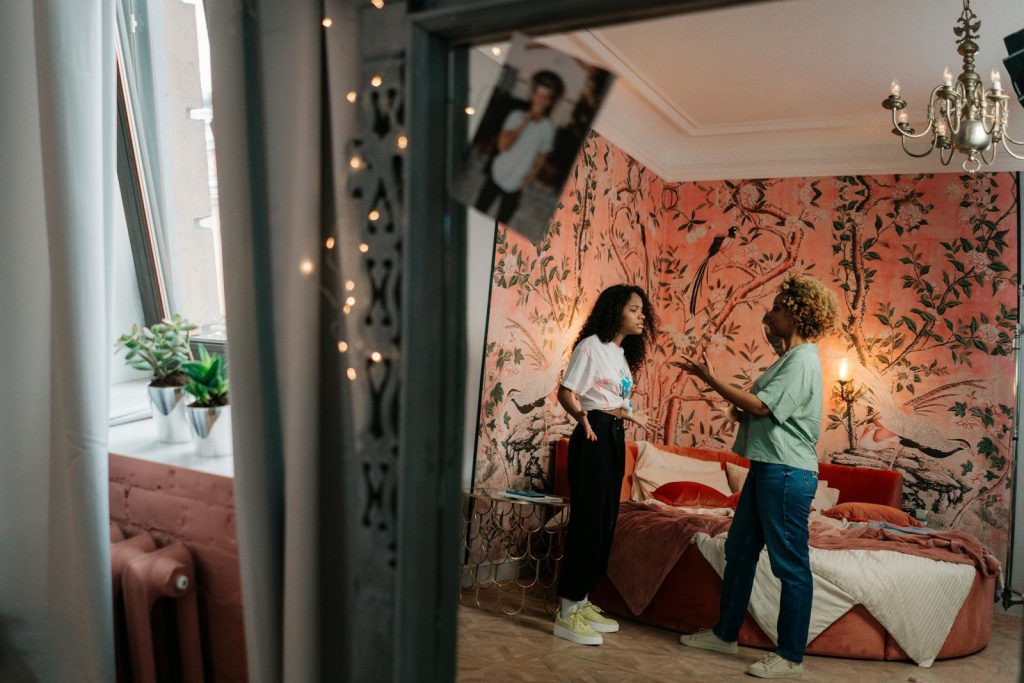 A mother and daughter engage in conversation in a cozy, decorated bedroom at home.