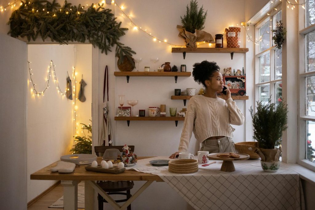 African American woman in cozy winter room with Christmas lights, talking on smartphone.
