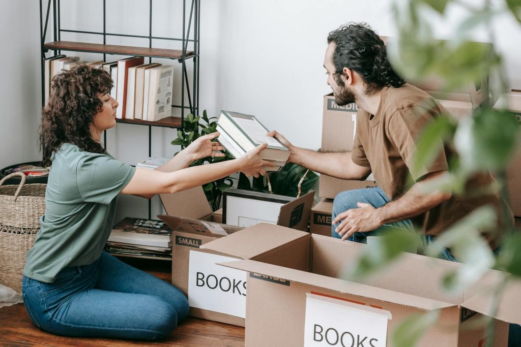 A couple organizing and packing books in cardboard boxes indoors, preparing for a move.