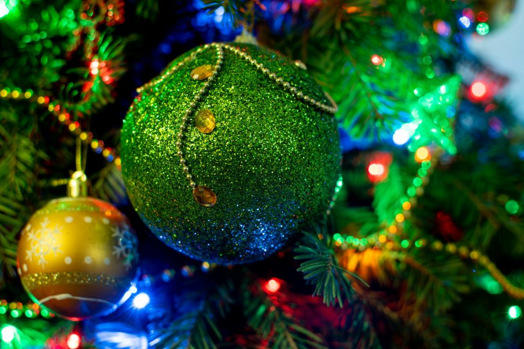A green christmas ornament hanging from a christmas tree
