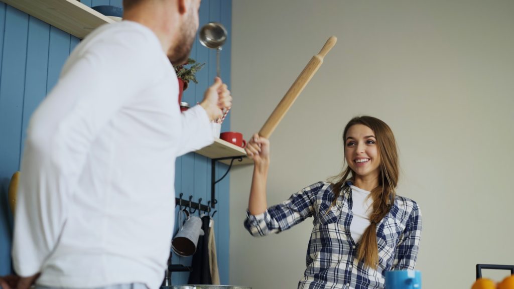 Couple playfully fighting with rolling pin in kitchen
