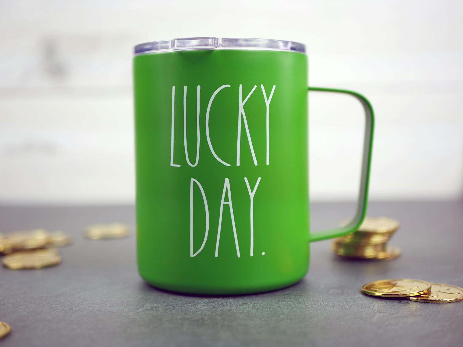 A green mug with 'Lucky Day' text, surrounded by coins, perfect for St Patrick's Day celebrations.