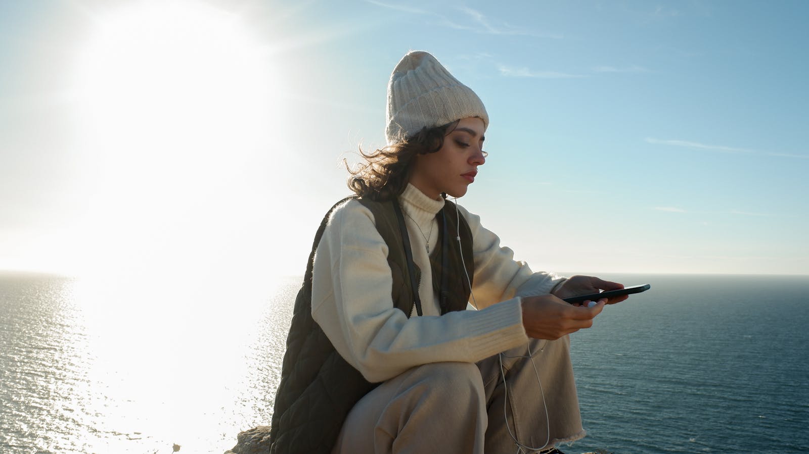 Serene moment of a woman enjoying music by the sea at sunset in Sesimbra, Portugal.