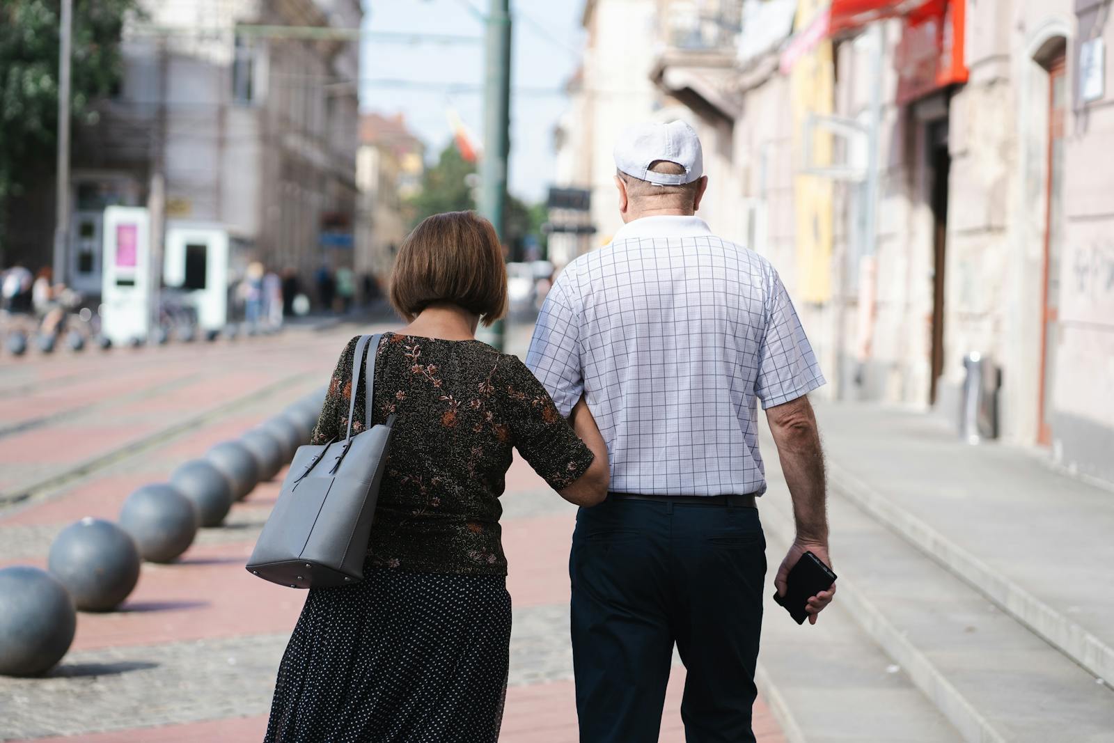 Senior couple walking arm-in-arm on a sunny urban street, capturing a moment of togetherness.