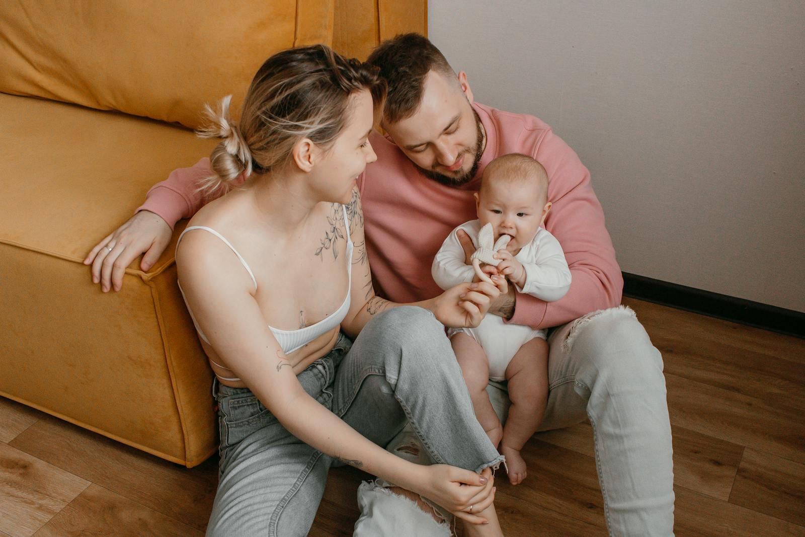 A happy family with their baby smiling and sitting on a sofa in a cozy living room.