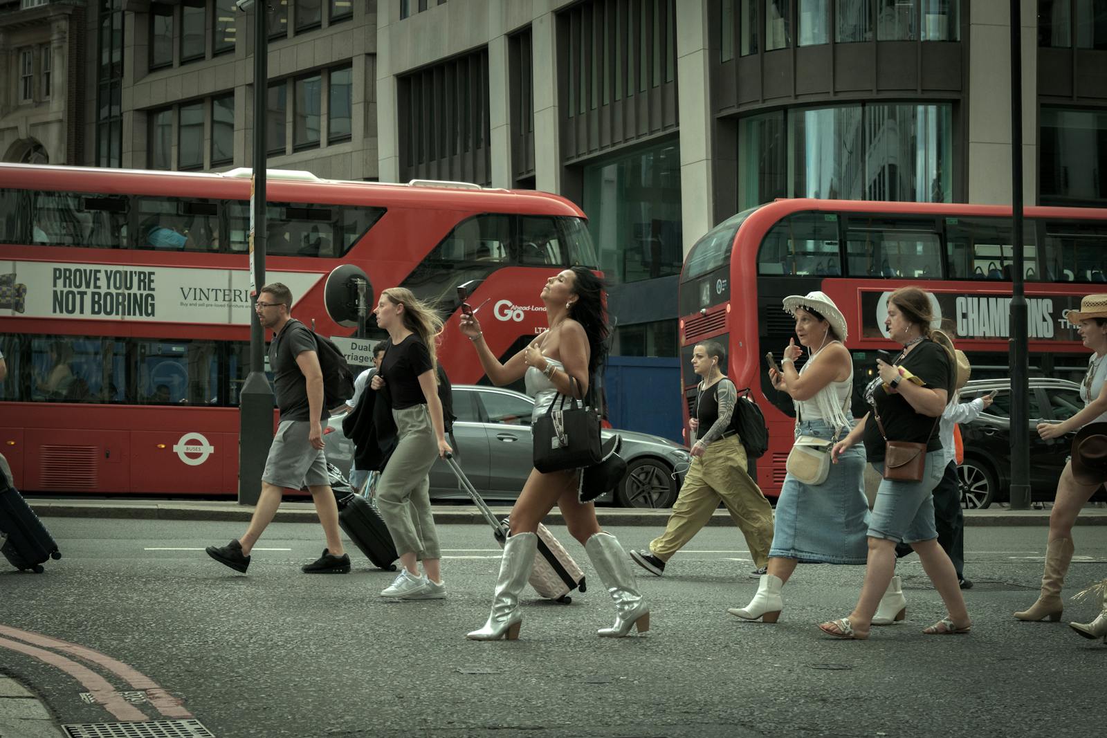 Crowd crossing a London street with iconic red buses in motion, capturing urban life.