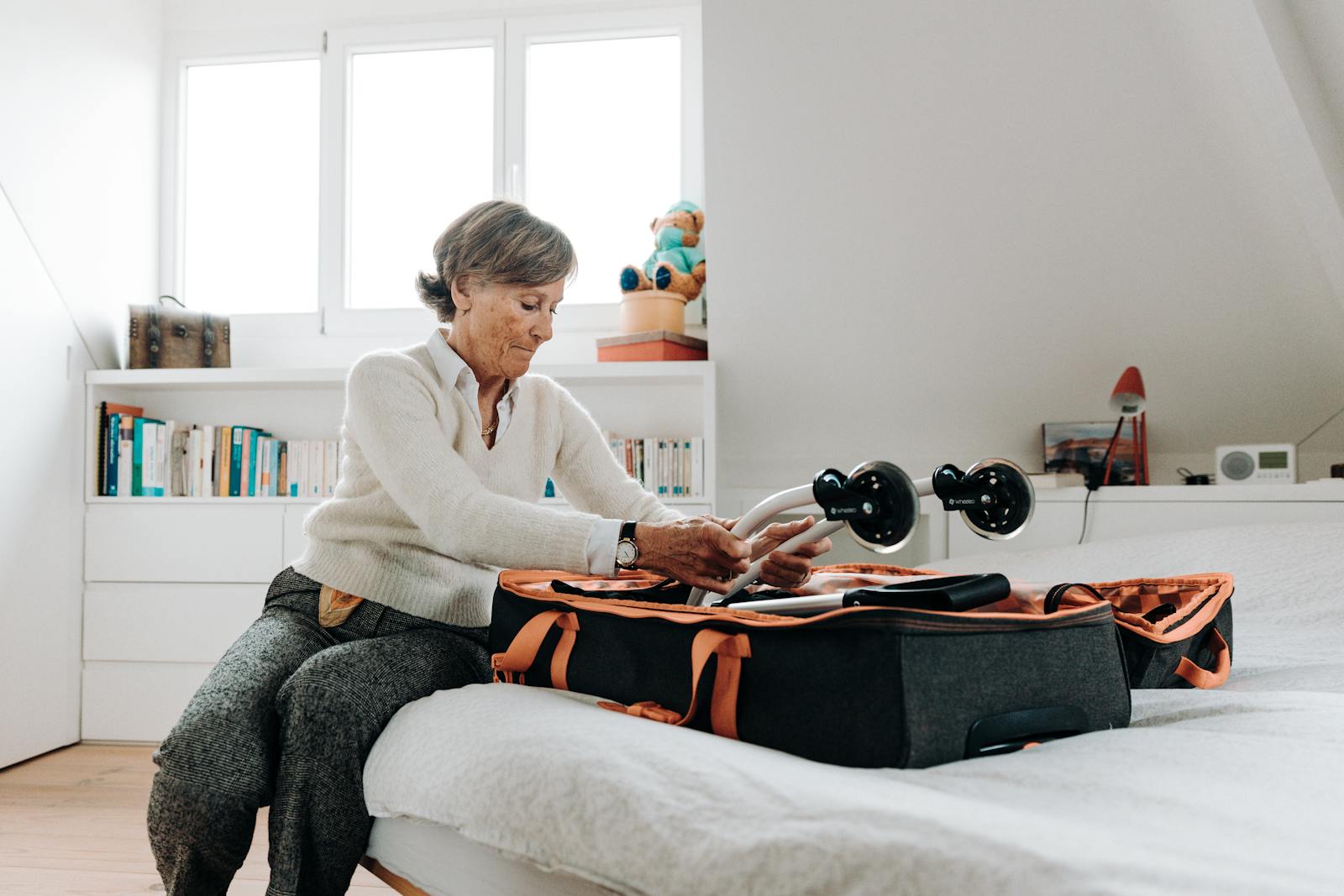 Senior woman packing a suitcase in a bright, modern bedroom setting.