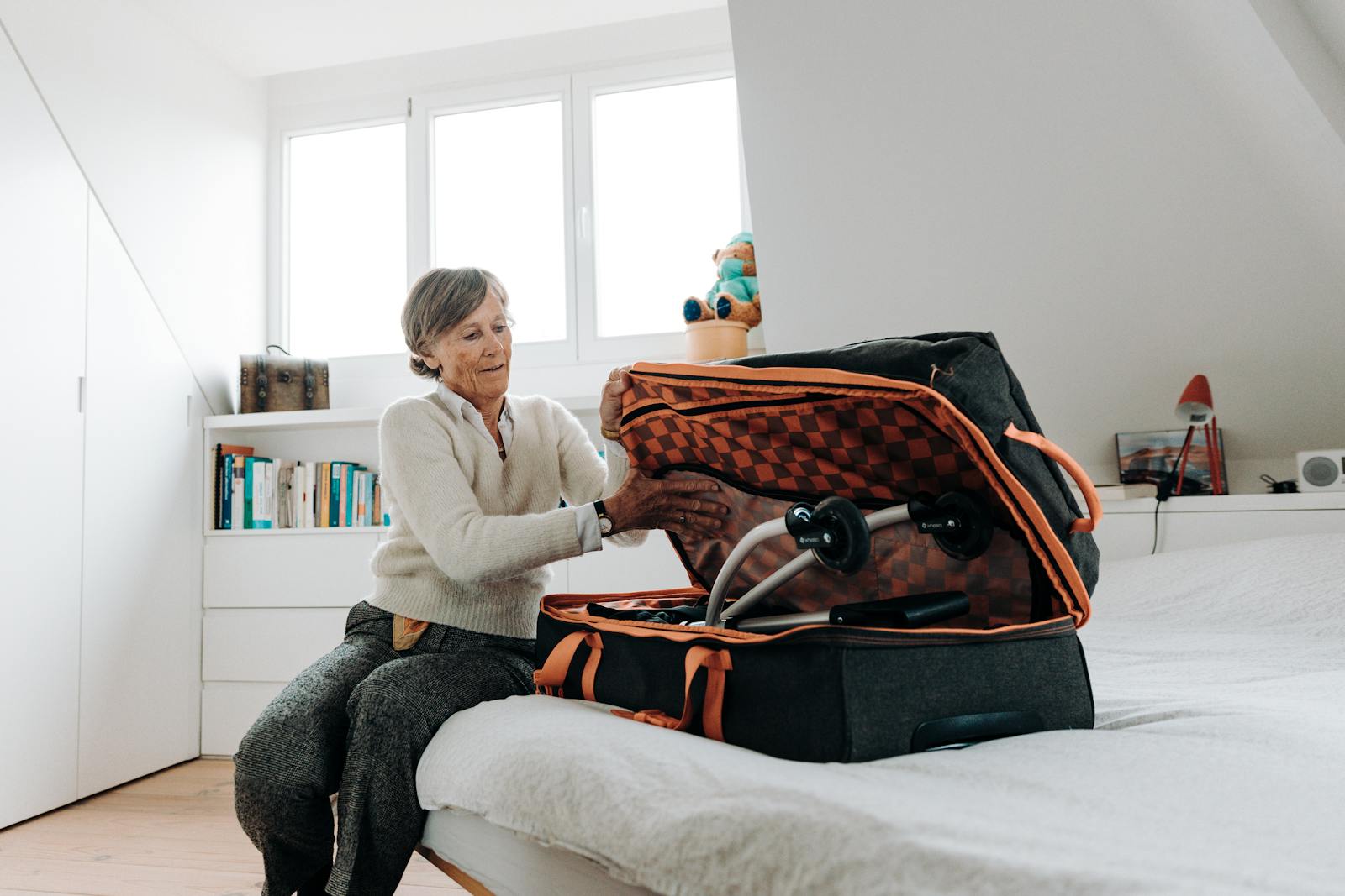 Senior woman packing a suitcase with a rollator in a bright, modern bedroom.