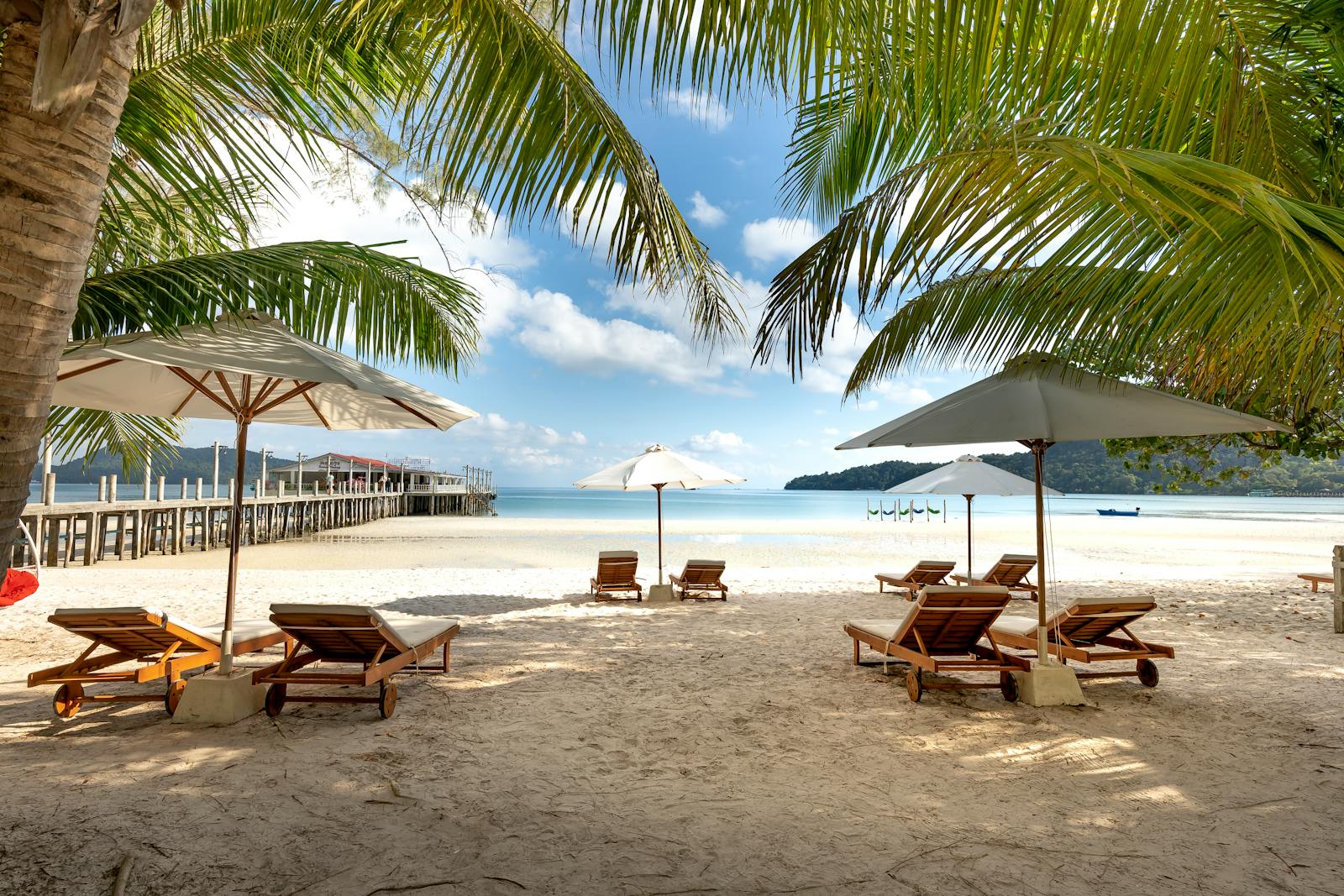Relaxing tropical beach view with palm trees, umbrellas, and lounge chairs on a sunny day.