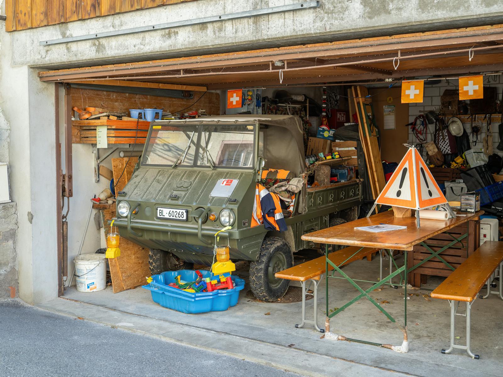 A military vehicle and various items in a crowded garage with Swiss decor.