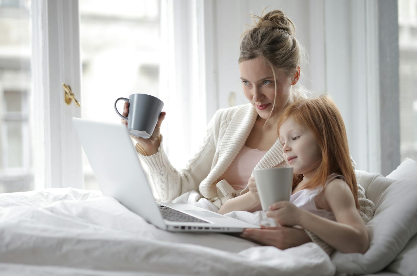 A mother and daughter enjoying a cozy morning together with coffee and a laptop.