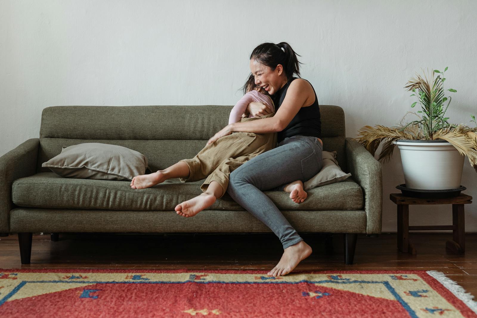 A happy mother and daughter laughing together on a cozy living room sofa.