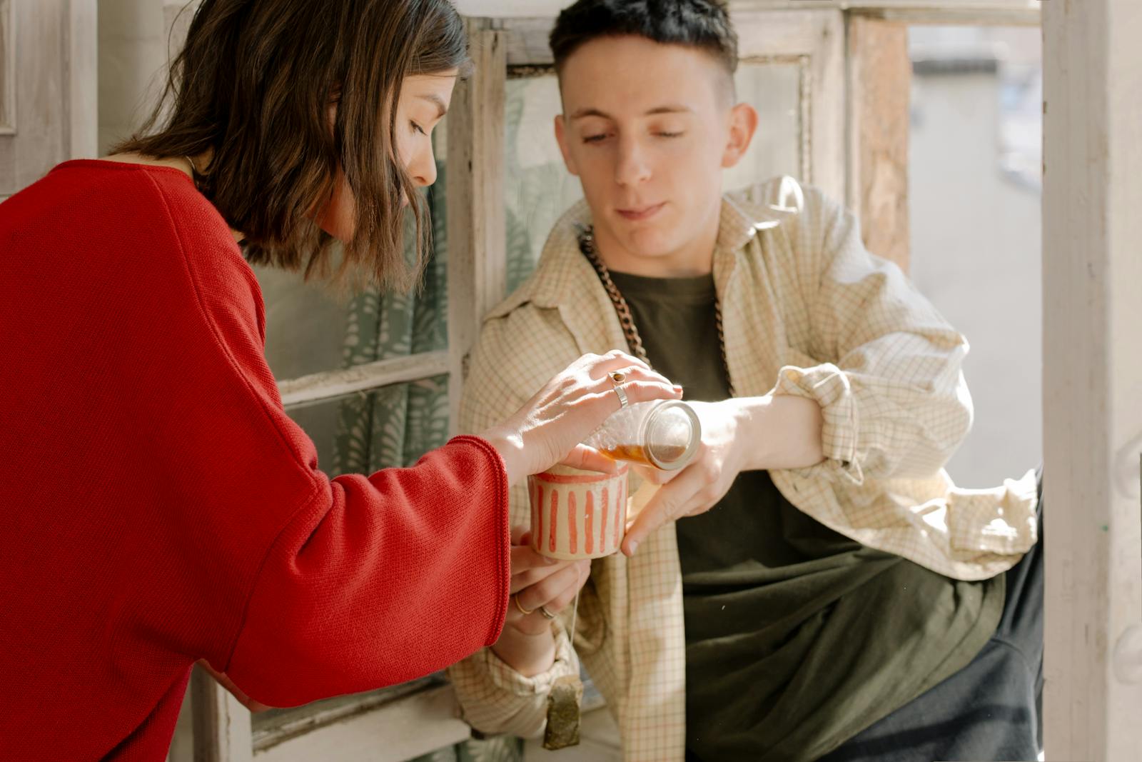 A young couple sharing tea by a window, evoking warmth and companionship indoors.