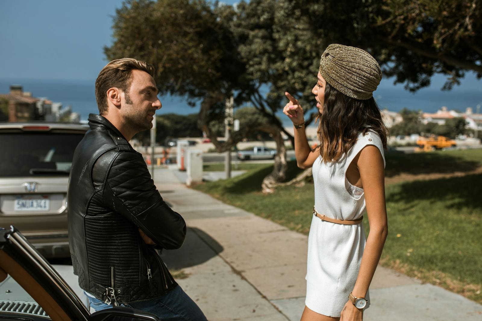 An interracial couple having an intense conversation near a park with an ocean view, expressing emotions vividly.