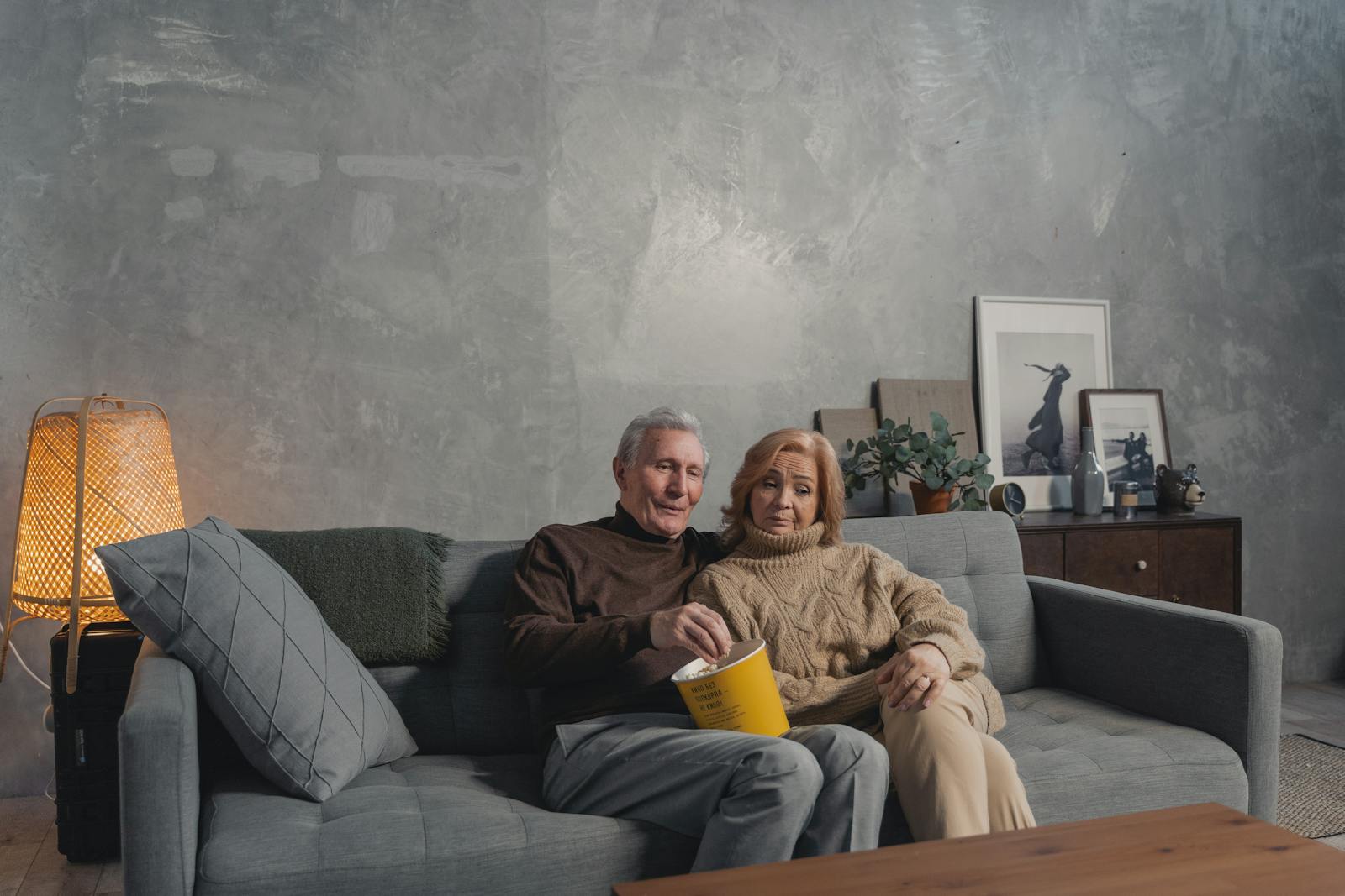Senior couple enjoying popcorn together on a cozy sofa in a warm living room setting.