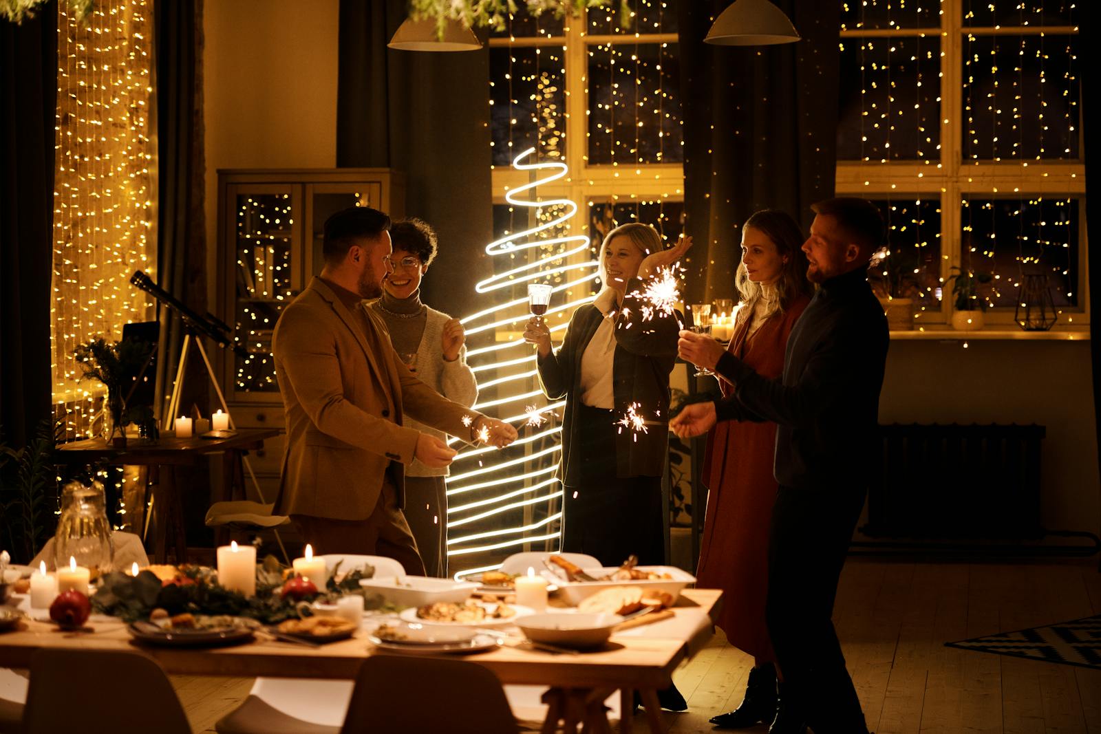Group of adults celebrating Christmas indoors with sparklers and festive decor.
