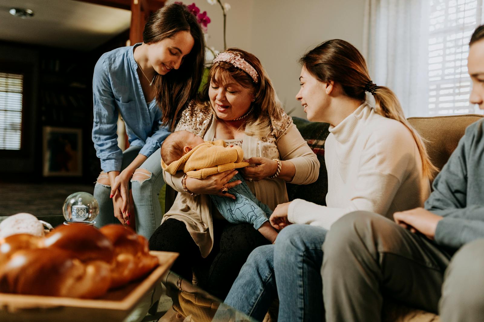 A touching family moment featuring a grandmother holding a baby surrounded by loved ones indoors.