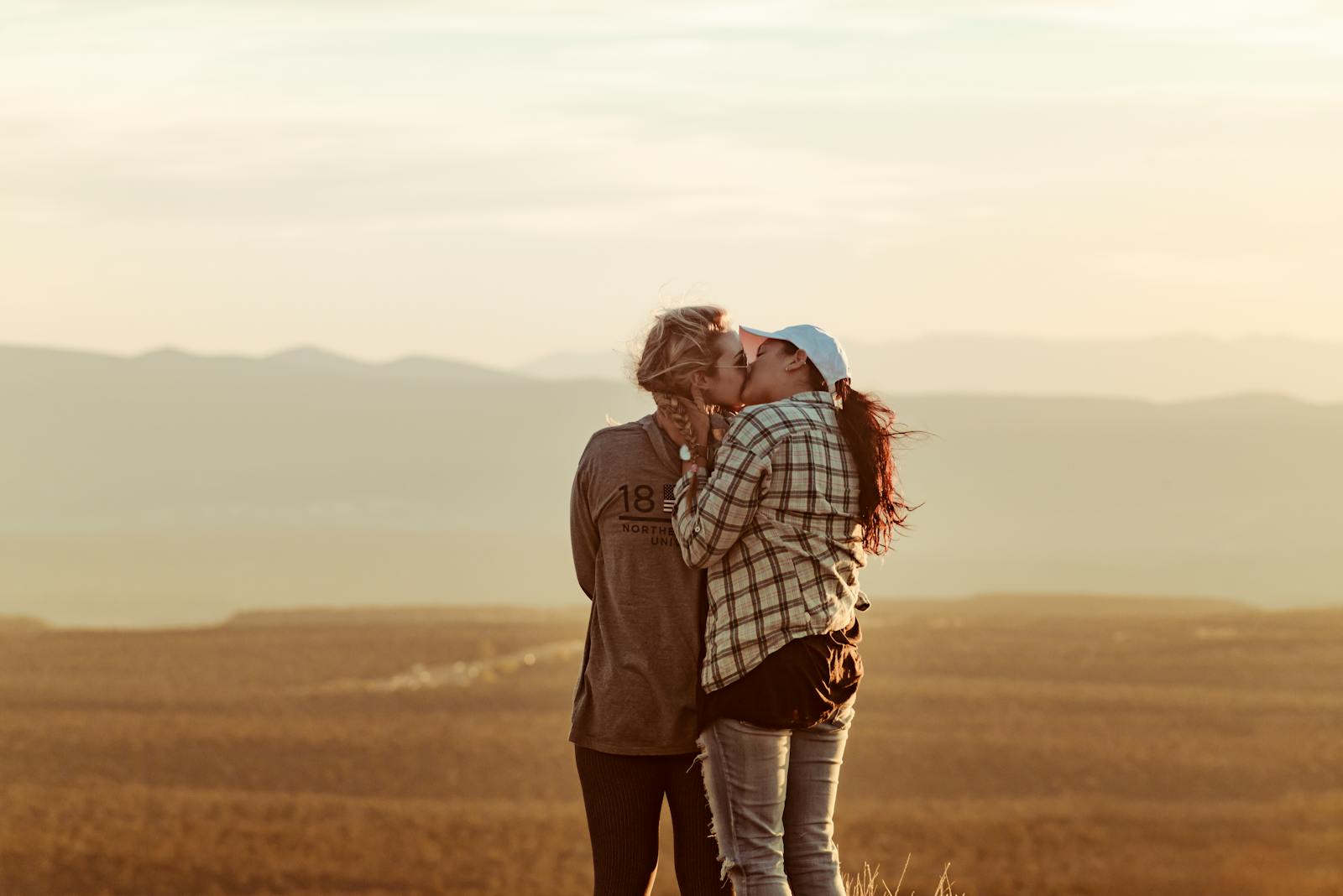 Two women share a romantic kiss against a stunning sunset backdrop, embracing love and togetherness.
