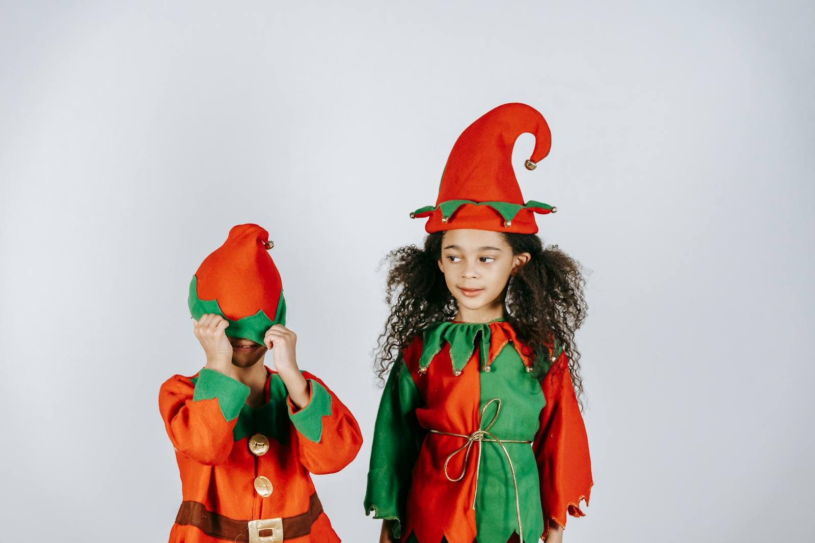 Two happy children in festive elf costumes enjoying a cheerful holiday moment indoors.