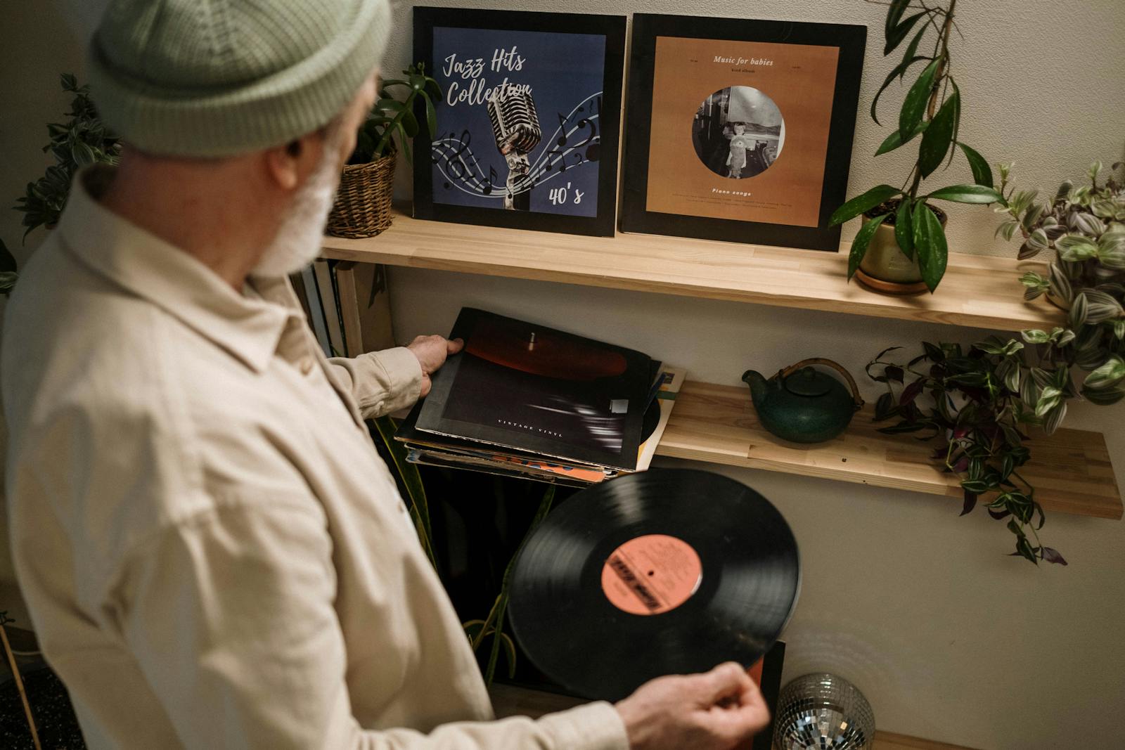 Elderly man browsing a collection of vinyl records indoors, surrounded by shelves and plants.