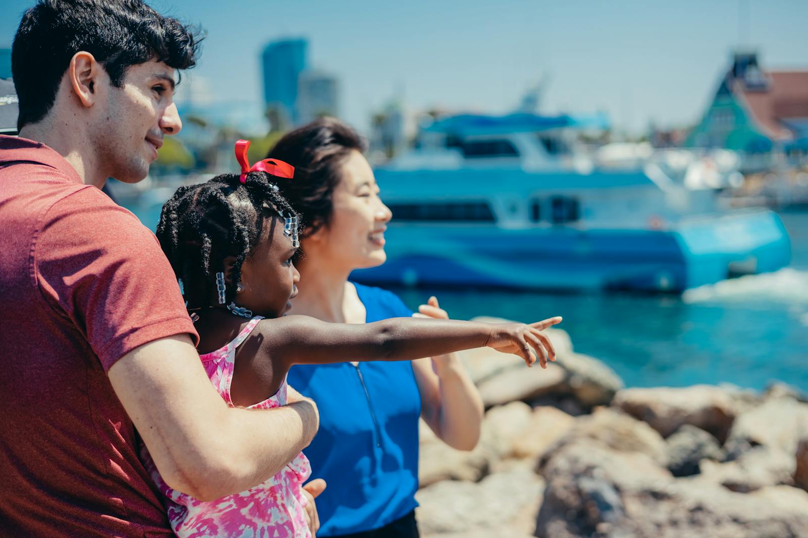 Multicultural family enjoying a sunny day by the waterfront, pointing at boats.