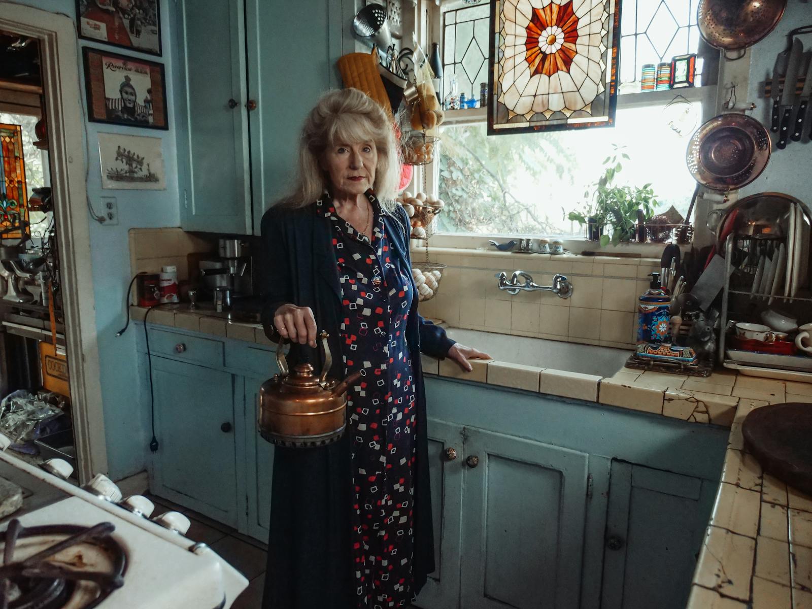 Elderly woman holding kettle in charming vintage kitchen setting.
