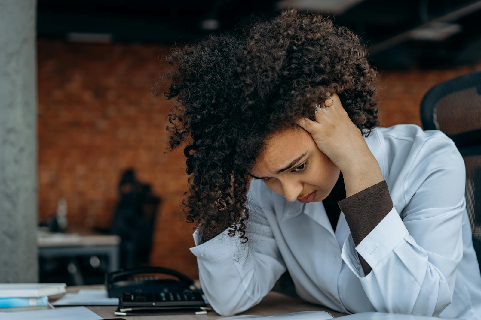 A woman in an office appears stressed while reviewing documents at her desk.