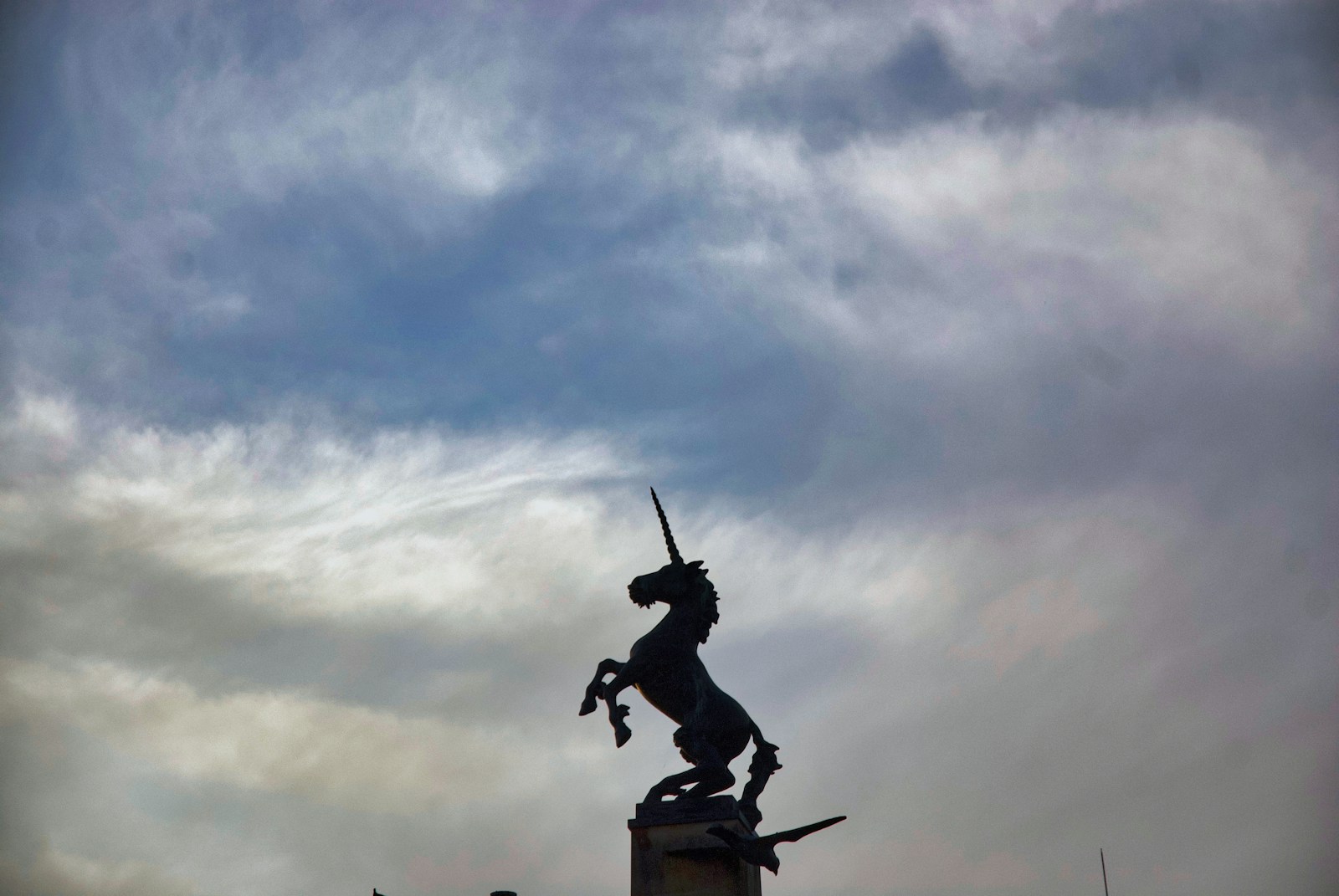 Silhouette of a unicorn statue against a cloudy sky