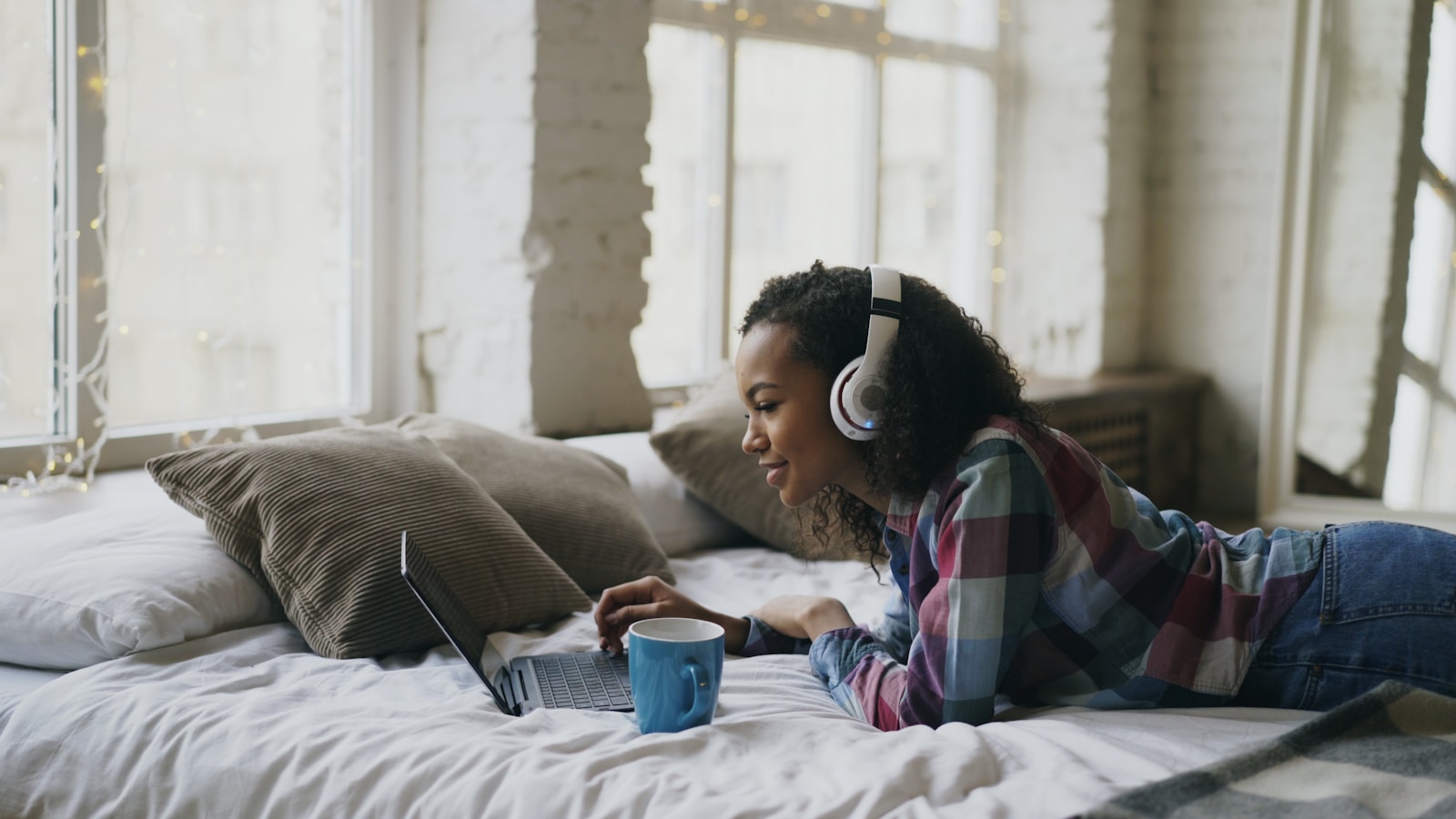 Woman with headphones using laptop on bed