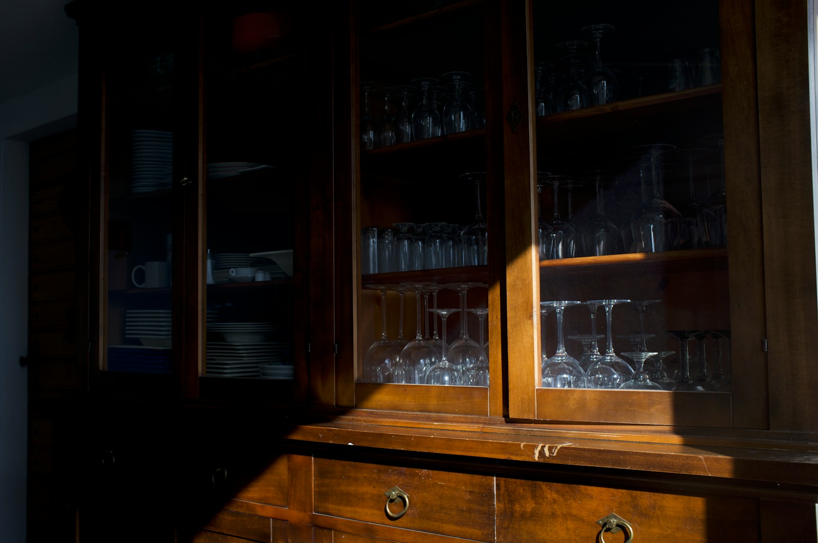Wooden cabinet with glassware illuminated by sunlight.