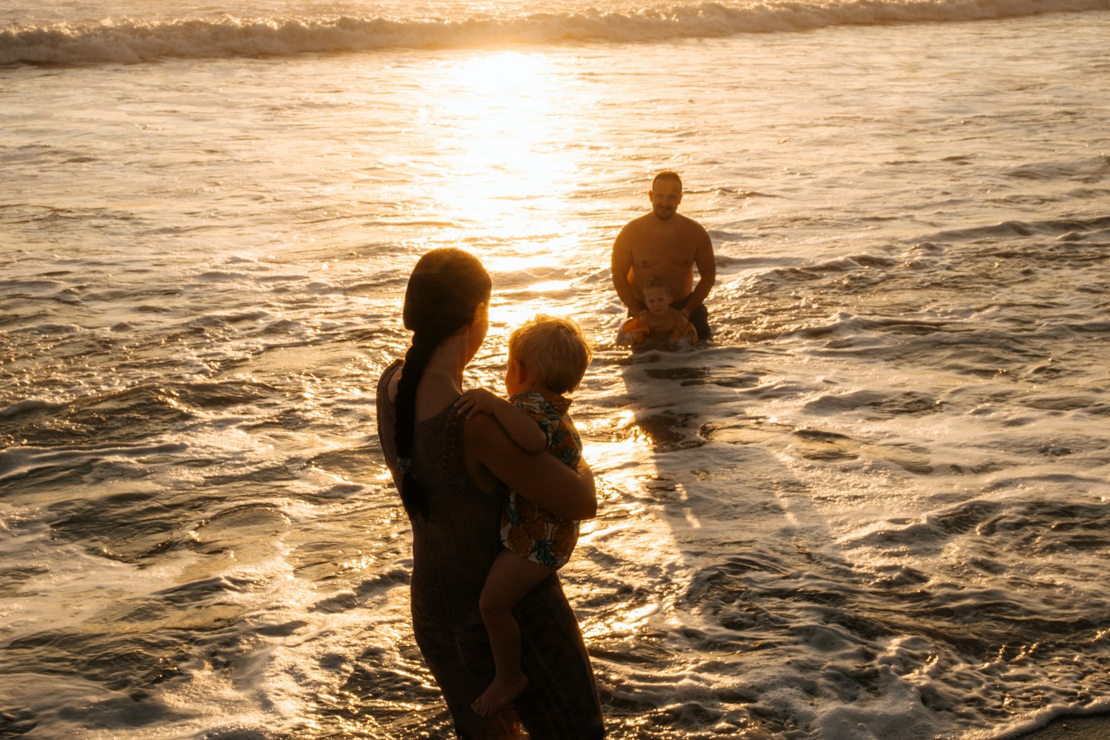 Family playing in the ocean at sunset