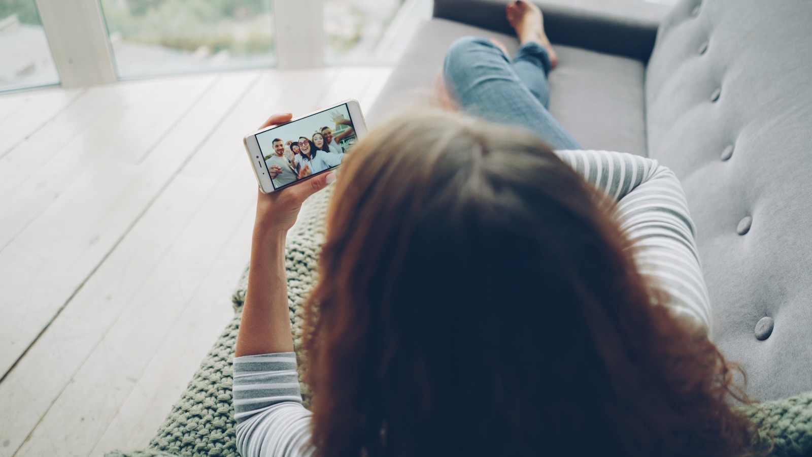 Woman watching video call on smartphone while relaxing on couch.