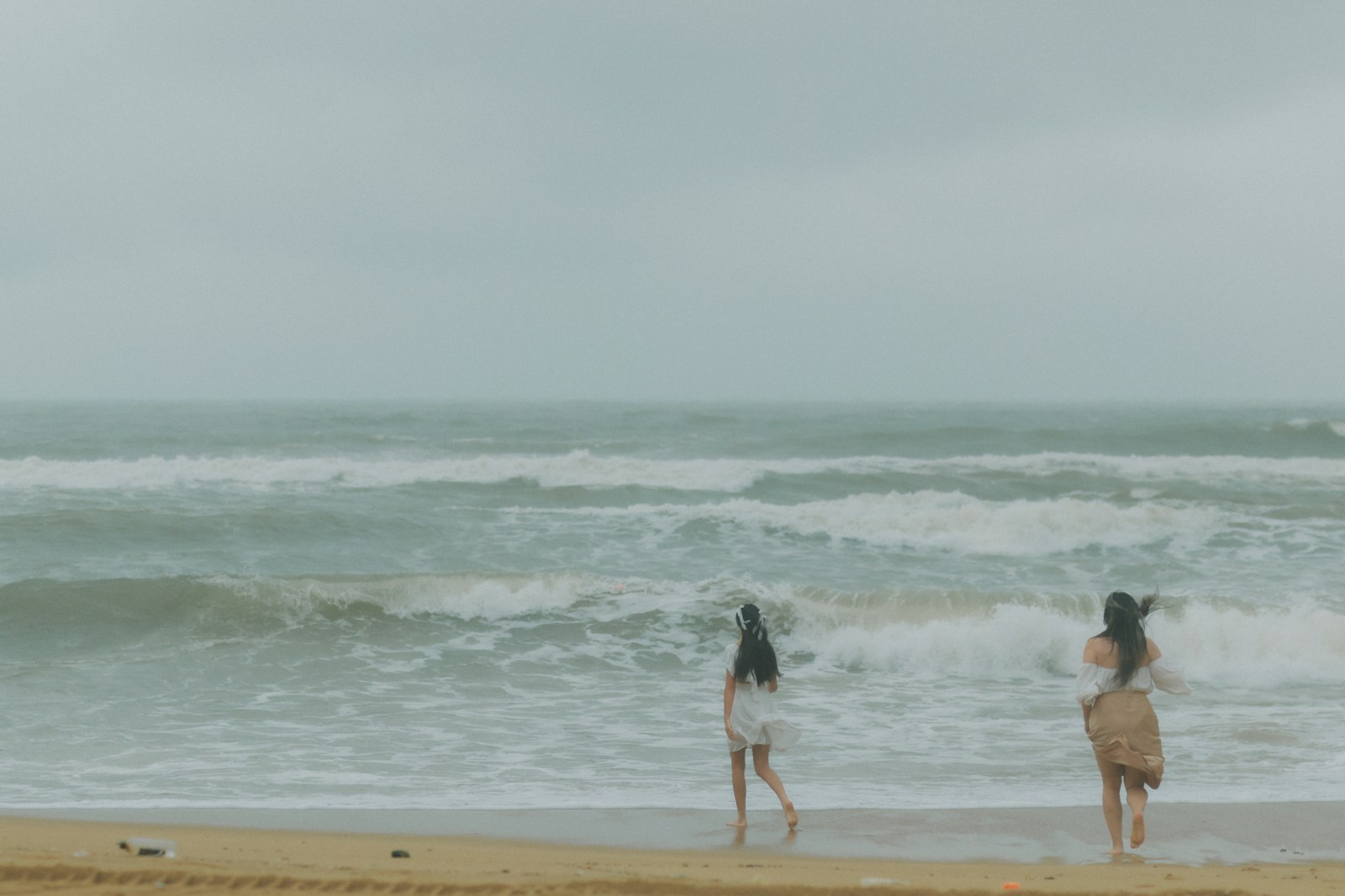 Two women walk on a sandy beach by the ocean.