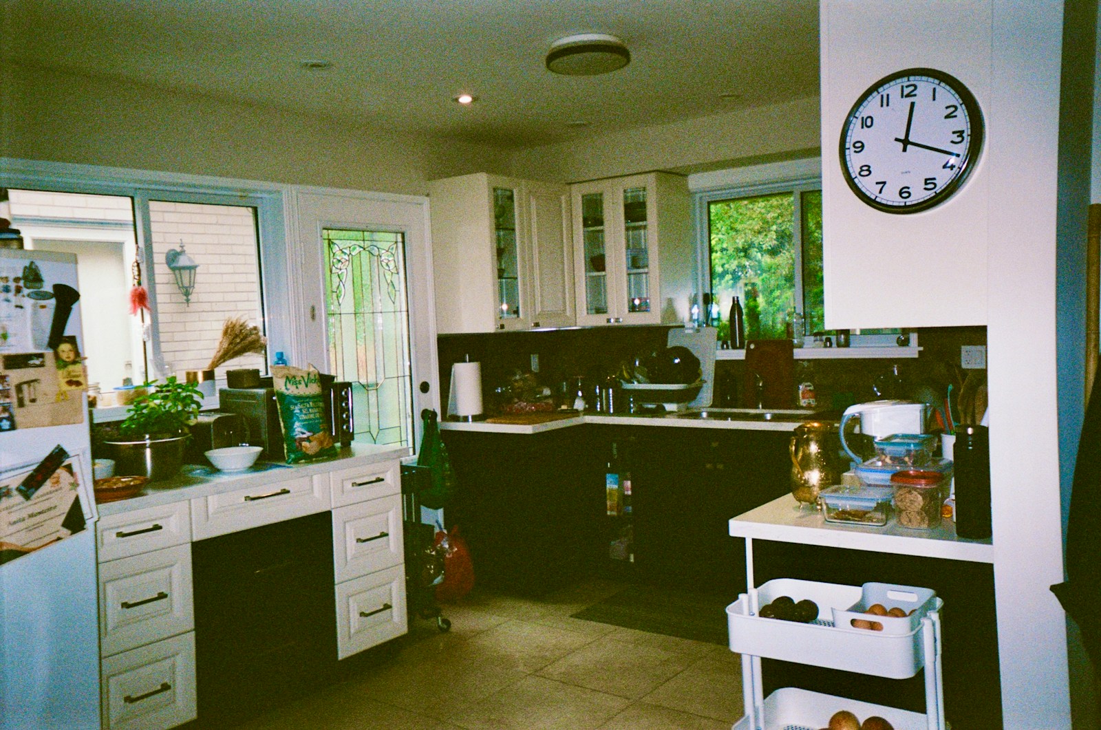 A kitchen is shown with a clock and cabinets.
