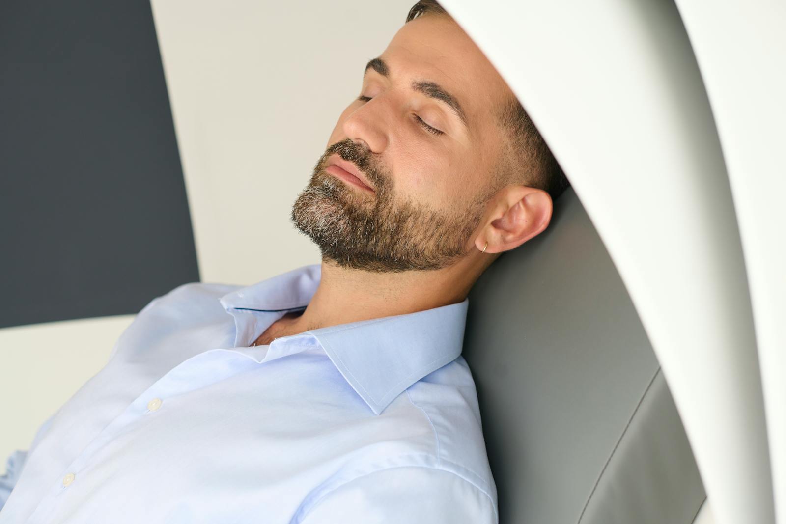 A bearded man wearing a blue shirt resting with eyes closed, conveys relaxation.