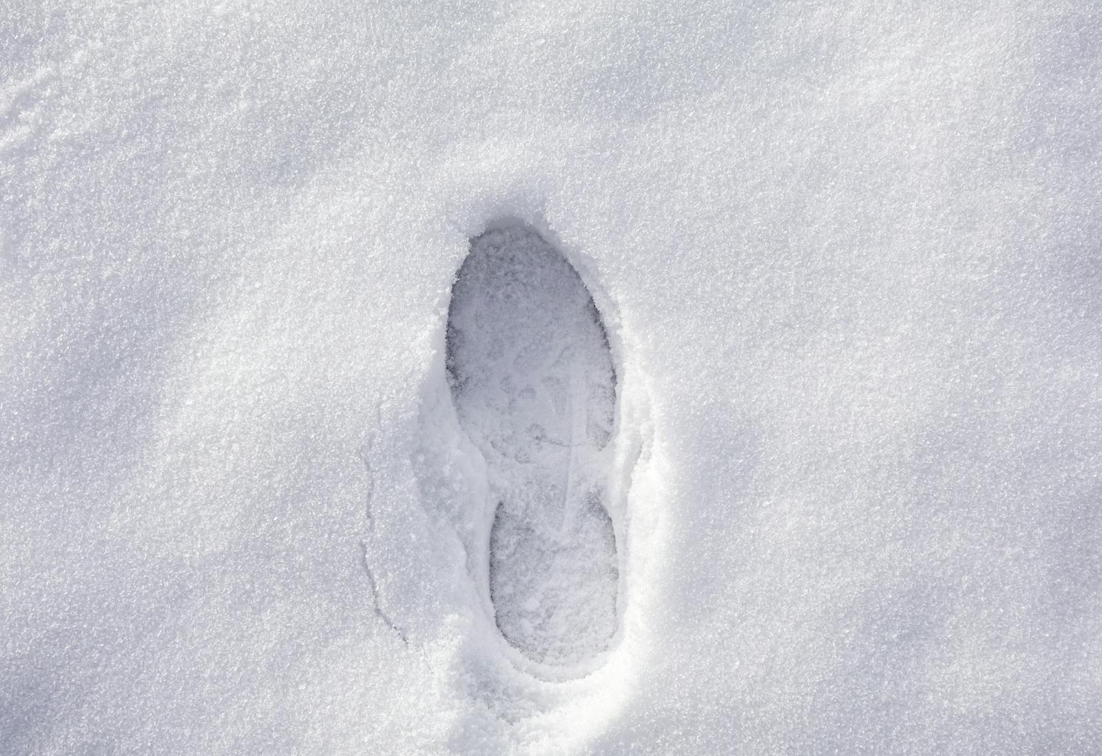 Close-up of a single footprint imprinted on pristine, untouched snow, showcasing winter's serene beauty.