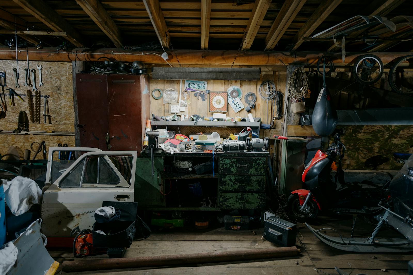 A cluttered garage interior with tools, motorcycle, and car door parts.