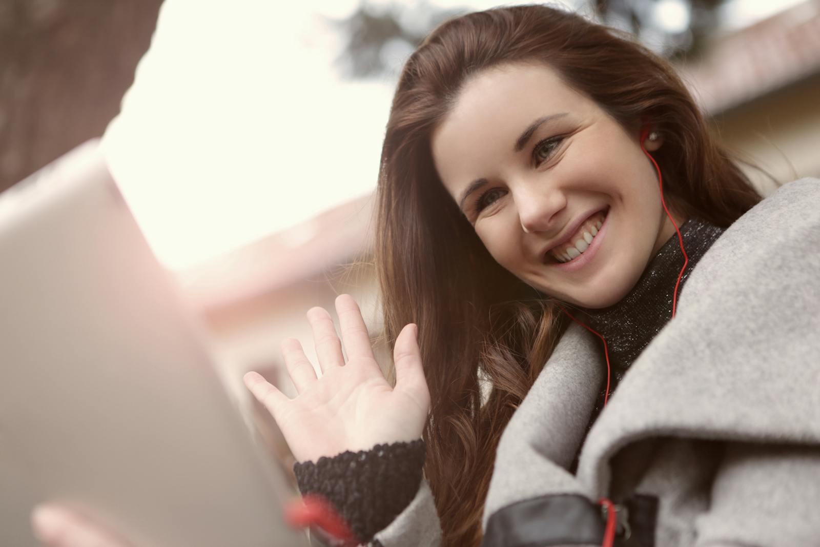 Young woman smiles and waves during an outdoor video call, showcasing modern wireless communication.